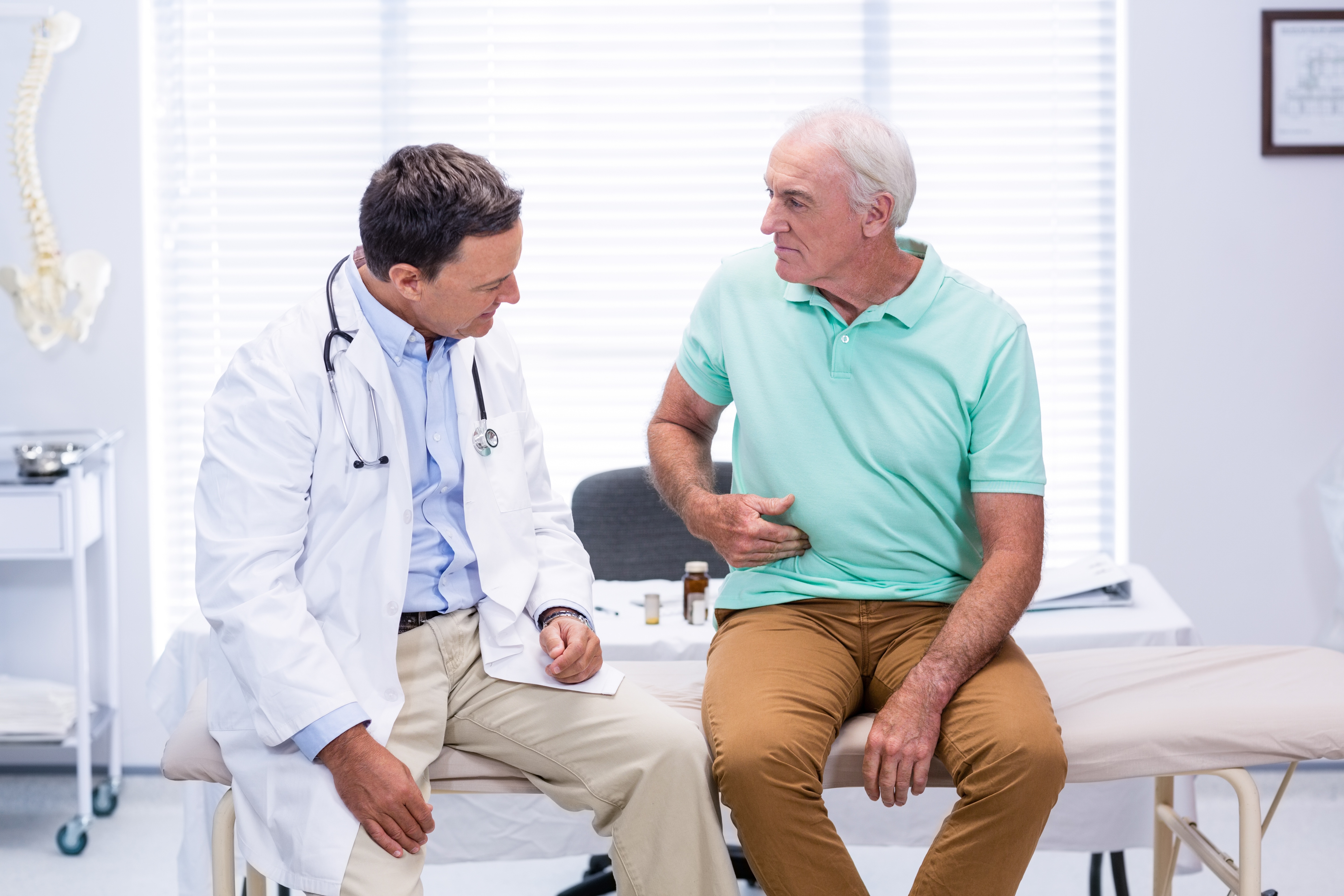 senior man showing stomach ache pain to gastroenterologist