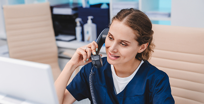 health care worker in scrubs sitting at a desk making a consultation over the phone