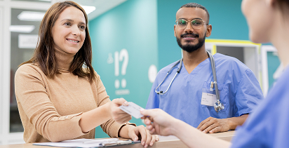 patient standing with the medical worker who has seen her while passing a payment card to an administrative professional