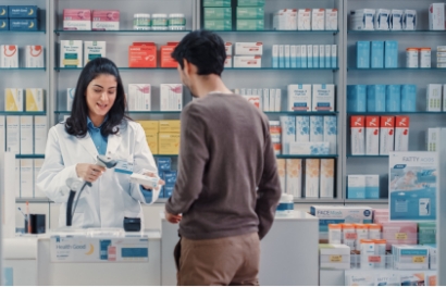 a pharmacist, facing the camera, checking out purchases for a customer whose back is turned to the camera