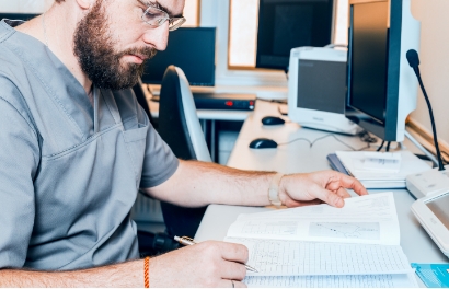 a bearded man in scrubs sitting at a desk reviews paperwork