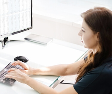 over-the-shoulder view of a woman in scrubs sitting at a computer typing